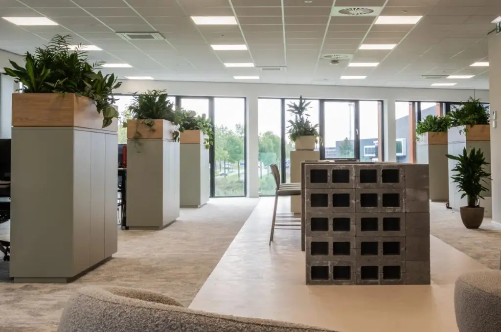 Open kantoor met groene roomdividers van plantenbakken op maat, die structuur en rust creëren volgens de principes van biophilic design.